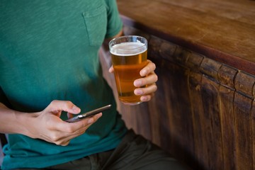 Midsection of man using phone while having beer