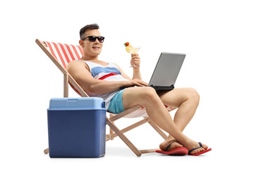 Young man with laptop and cocktail sitting in a deck chair