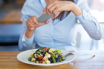 Woman with smartphone photographing food at cafe
