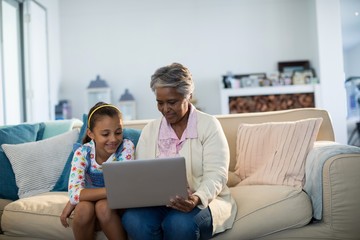 Grandmother and granddaughter using laptop in living room