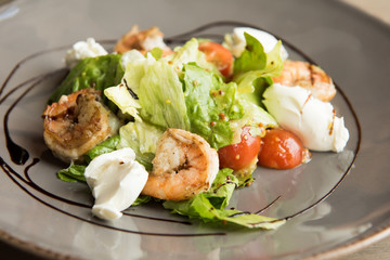 Restaurant healthy food, salad, arugula with shrimps and cherry tomatoes, covered with parmesan, closeup at plate