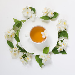 Jasmine leaves and flowers around cup of green tea on white background. Top view and concept.