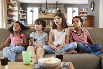 Group Of Children Sitting On Sofa Watching Television Together