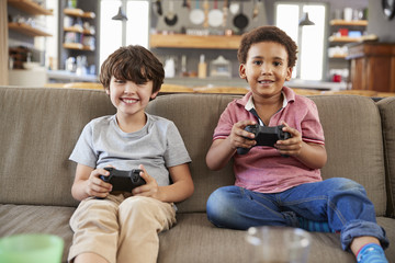 Obraz premium Two Boys Sitting On Sofa In Lounge Playing Video Game Together