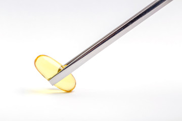 Close up a soft gel capsule is holding by metal chopsticks with white background, essential oil and healthcare concept.