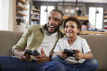 Father And Son Sitting On Sofa In Lounge Playing Video Game