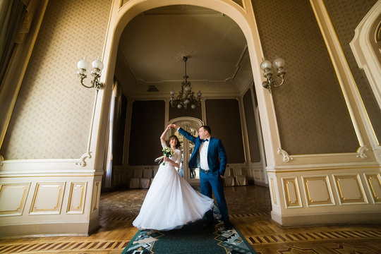 Horizontal photo of the happy newlyweds dancing in the old baroque castle.