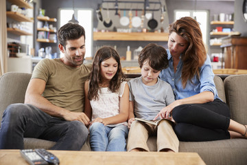 Family Sitting On Sofa In Lounge Reading Book Together