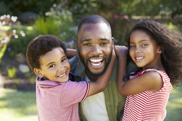 Fototapeta premium Portrait Of Father Carrying Children In Garden