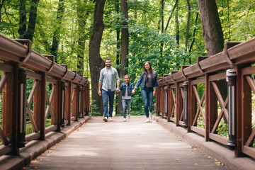 Fototapeta na wymiar young interracial family holding hands and walking through the wooden bridge in forest