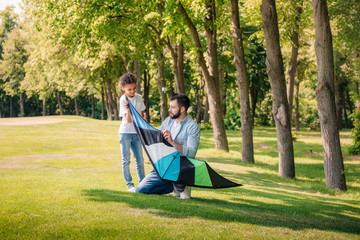father helping daughter with kite while spending time together in park