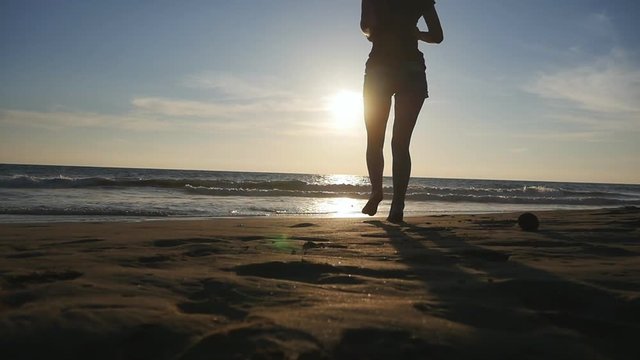 Young woman running on beach to the ocean at sunset. Beautiful young girl going on shore to the sea during vacation. Relax on summer holiday. Rear back view Slow motion