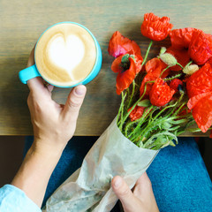 Bouquet of poppy flowers and a cup of cappuccino in woman hands. Summer concept