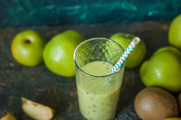 Green apples and kiwi on a wooden tray on a dark textural background. A glass of apple juice with a straw. A glass of kiwi juice with a straw. Healthy eating. Fruits, detox