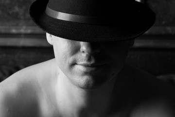 Man in a black hat with naked shoulders. Black and white. Selective focus.