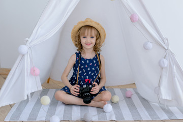 beautiful girl in a hat sitting in a white wigwam with a garland of balls and holding an old camera. © NATALYA