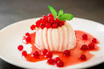 Panna cotta with currant berries in white plate on a dark table. Traditional Italian dessert.