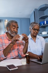 Man looking at medicine while sitting by woman using laptop computer