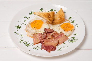 Plate of breakfast with fried eggs, bacon and toasts isolated on white background