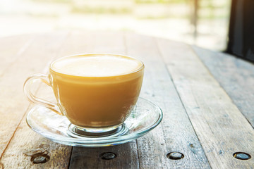 Hot coffee in glass cup on old wooden desk , warm light tone