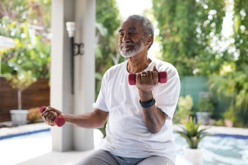 Senior man lifting dumbbell while exercising - Powered by Adobe