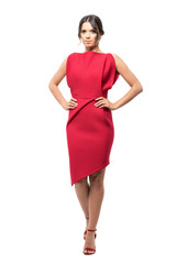 Gorgeous young woman in red dress posing with hands on hips looking at camera.  Full body length portrait isolated on white studio background. 