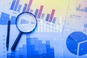 Magnifying glass and documents with analytics data lying on table,selective focus