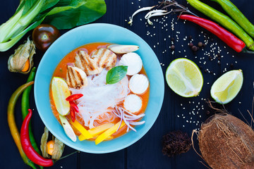 Delicious thai tom yam soup with funchoza noodles, grilled chicken and vegetables, served in blue plate