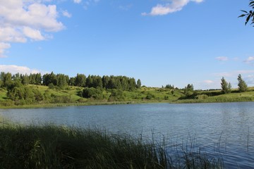 The lake is in good sunny weather. The water is riddled with a slight ripple. The shores of the lake are covered with luscious green vegetation.