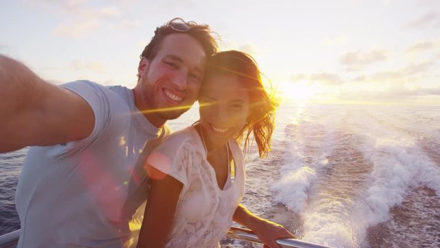 Selfie video - Romantic couple taking selfie video by sunset over the ocean on small cruise ship sailing on open sea. Woman and man taking cell phone photos on boat travel sailing during vacation.