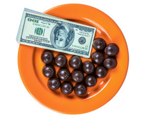 Hundred dollar banknotes and chocolate candies on an orange plate isolated on a white background 