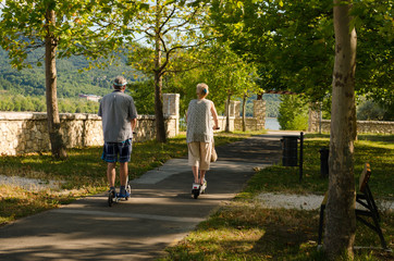 older couple riding electric roller in park. happy old people rollerskating on beach in summer