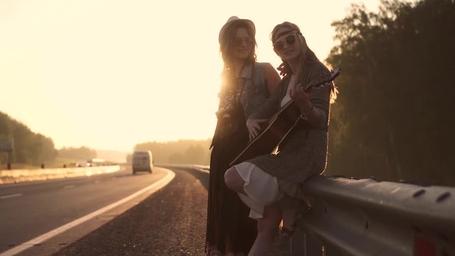 girls hippie sing songs and you play the guitar. two hipsters on the roadway at sunset