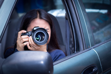 Young woman stalking and taking pictures with her camera, inside of her car