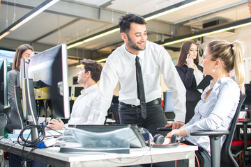 Businessman leaning over female colleague's desk  flirting in office while working on project together.