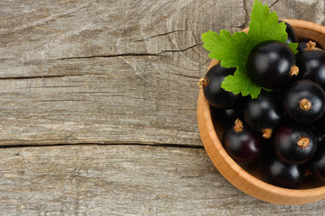 black currant in wooden bowl with green leaf on old wooden background. top view