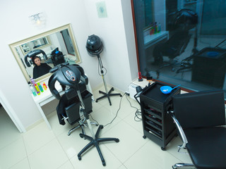 Woman in hairdresser, drying hair under machine
