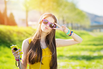 Cool teenage girl with smart phone and headphones outdoors in summer posing