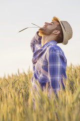 Young guy in the middle of the field with straw on his mouth and hat on head