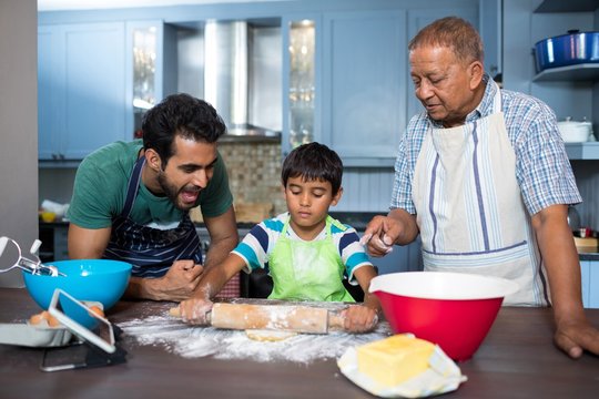 Father shouting with son rolling dough while standing by grandfa