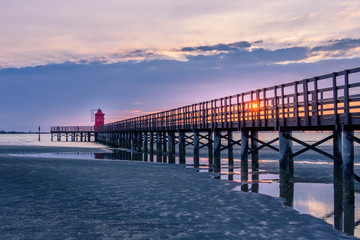 Beautiful sunrise at the seaside in Italy, at Lignano Sabbiadoro, with pier and lighthouse in the foreground.