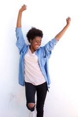 Excited young african woman standing with her arms raised against white wall