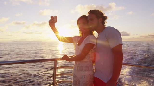 Cruise ship - Romantic couple taking selfie at sunset over the ocean on small cruise ship sailing on open sea. Woman and man taking cell phone photos on boat travel sailing during vacation.