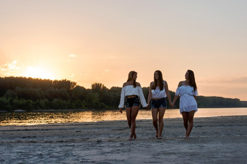 Fototapeta premium Three girls walking on the beach in the sunset