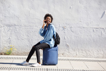 Afro american female sitting on suitcase outdoors and talking on mobile phone