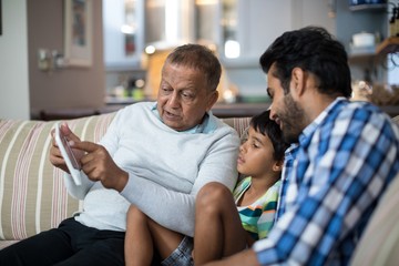 Grandfather showing tablet to grandson sitting with father at ho