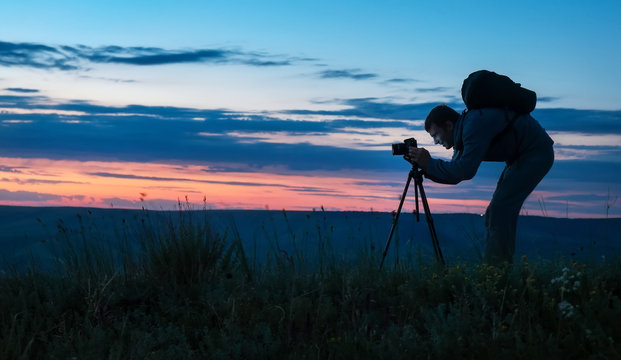 Silhouette of a professional photographer using a tripod, taking a photo of a mountain landscape