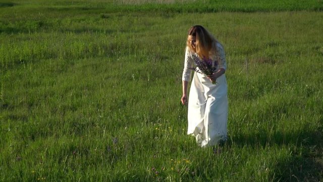 Beautiful young woman gathering flowers on the meadow