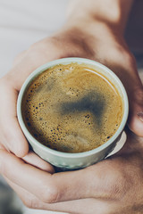 Closeup of tasty coffee espresso with tasty yellow foam in green ceramic cup. Male hands holding warm hot drink. Toning.