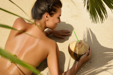 Woman with coconut drink under palm leaf